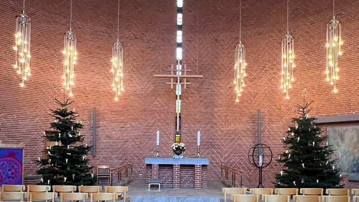 Elegant kirkeinteriør med festlige lys, pyntede juletræer og træbænke, der fører hen til et alter.