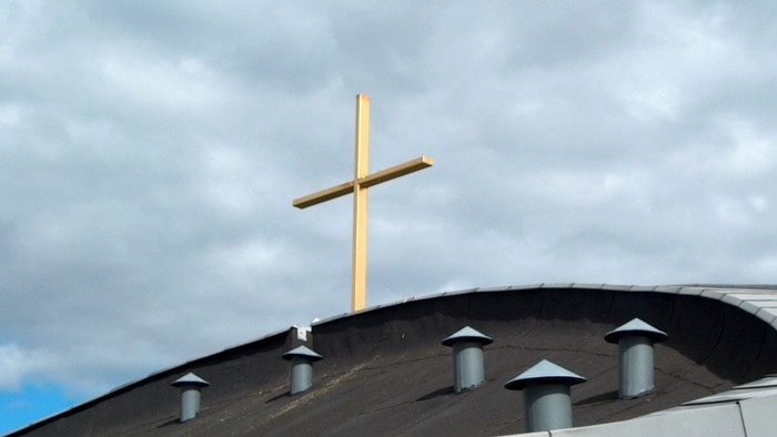 En stor gul kors på toppen af et sort tagtårn mod en skyeret himmel
