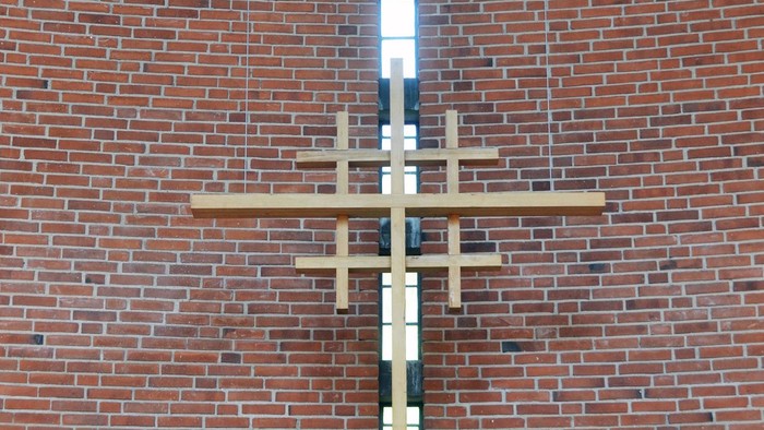 En stor korsformig lyskæde hænger på en mur af røde mursten.