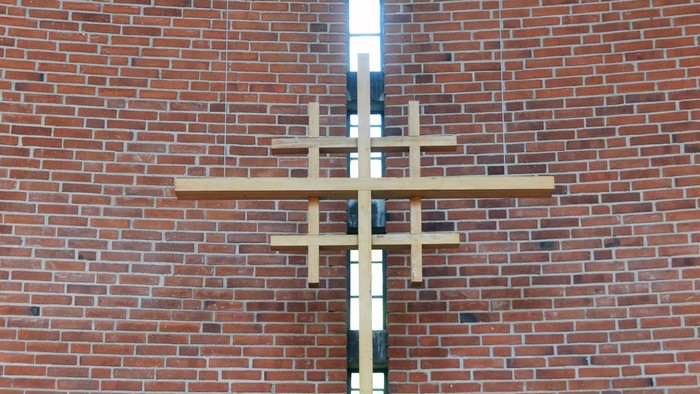 En stor korsformig lyskæde hænger på en mur af røde mursten.