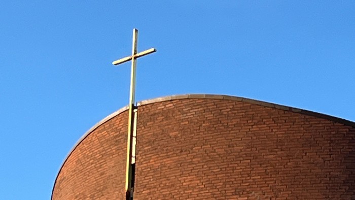 En stor mørk murstenskirke med et guldæret kors på toppen.