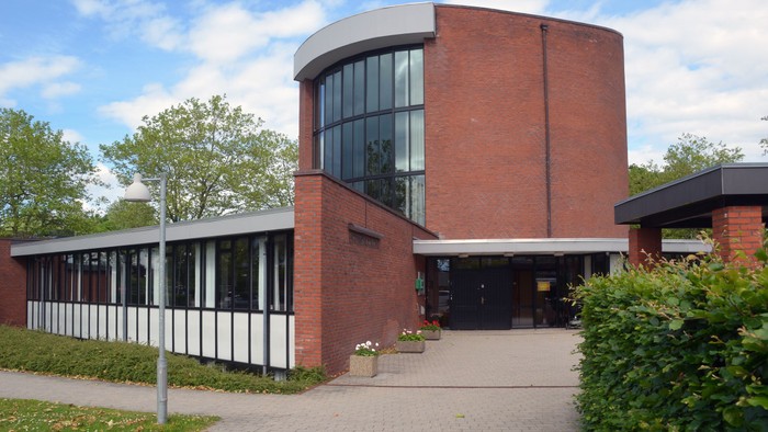 Et moderne bygning med røde mursten og store glaspartier, omgivet af græs og buske