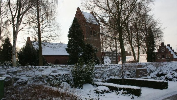 En snedækket park med træer og en røde murstensbygning i baggrunden