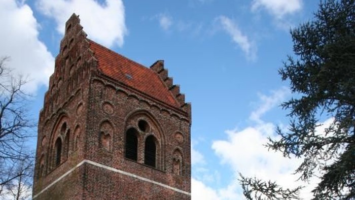 Røde murstenskirke med klokketårn og røde blomster.