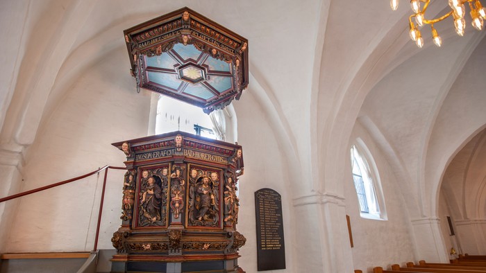 En prædikestol med udsmykning i en kirke med hvidt tagt.