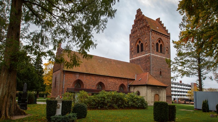 Historisk murstenskirke med højt tårn omgivet af en rolig, anlagt kirkegård.