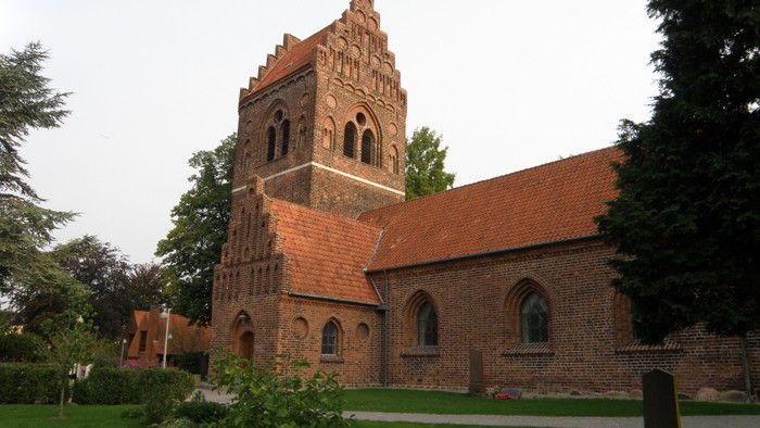 En gammel kirke med teglmur og tårn i en parkagtig omgivelse