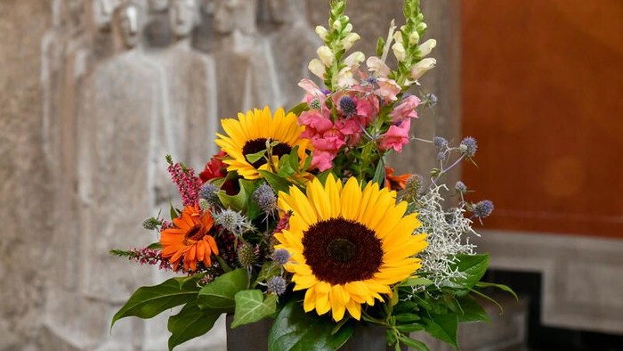 Ein Blumenstrauß mit Sonnenblumen und bunten Blumen vor einer Steinstatue.