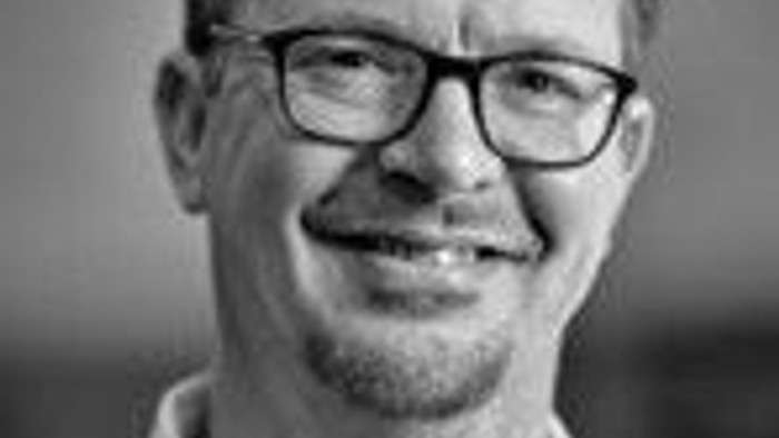 En svart-hvid portrætfoto af en mand med briller og kort hår.