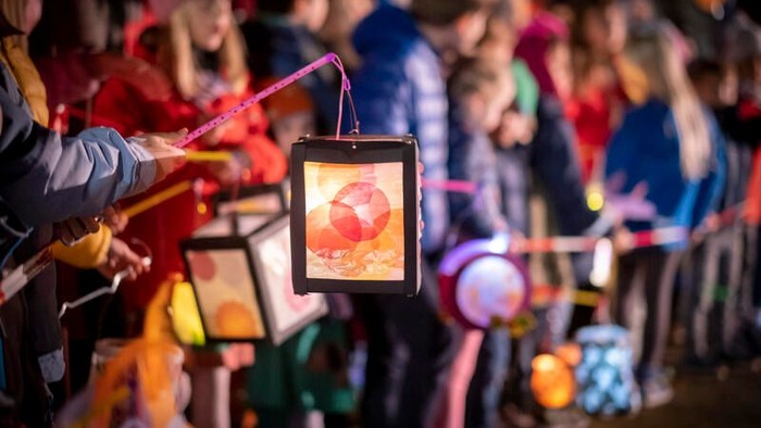 Eine Person hält ein Tablet mit einem leuchtenden Bild, umgeben von einer farbenfrohen Menschenmenge.