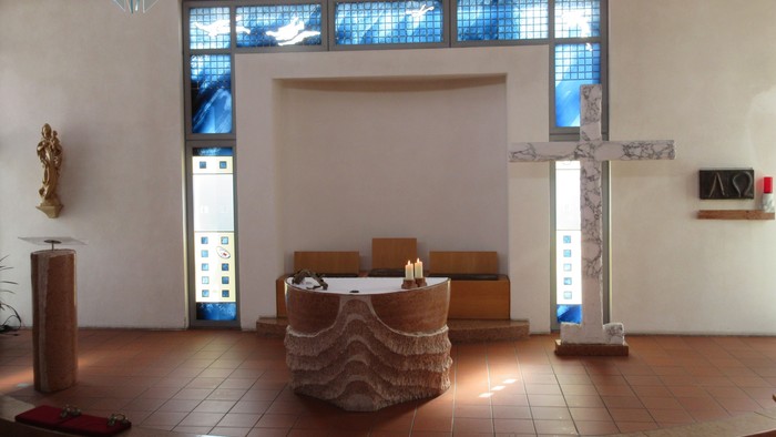 Ein runder Altar mit zwei brennenden Kerzen vor einem großen Kreuz aus Marmor.