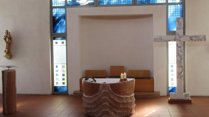 Ein runder Altar mit zwei brennenden Kerzen vor einem großen Kreuz aus Marmor.