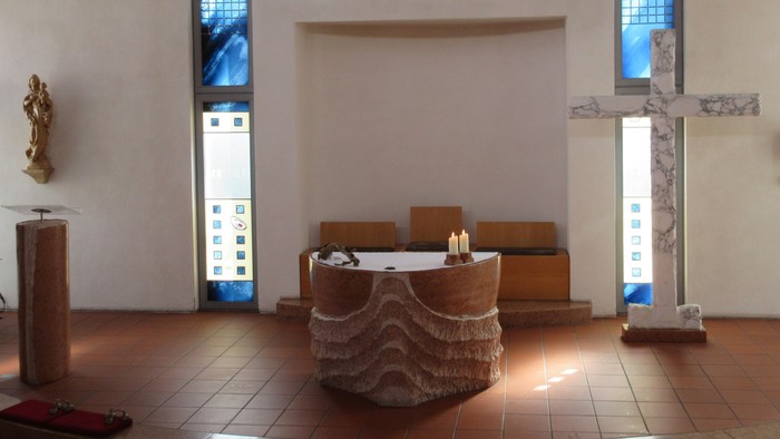 Ein runder Altar mit zwei brennenden Kerzen vor einem großen Kreuz aus Marmor.