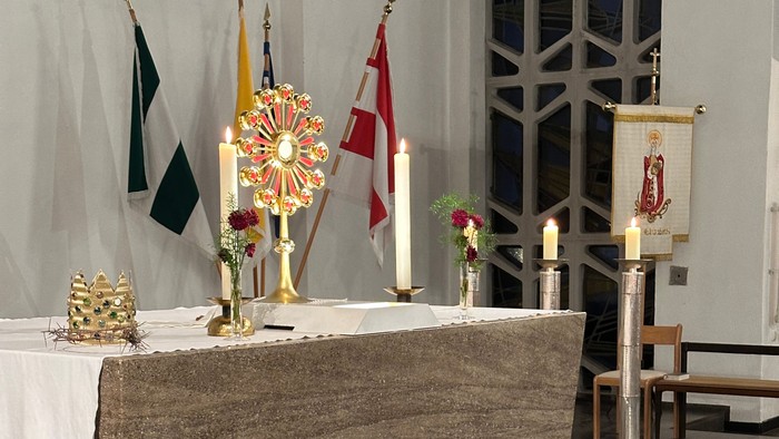 Eleganter Kirchenaltar, geschmückt mit Kerzen, Fahnen, Blumengestecken und religiösen Verzierungen auf einem Marmorboden.