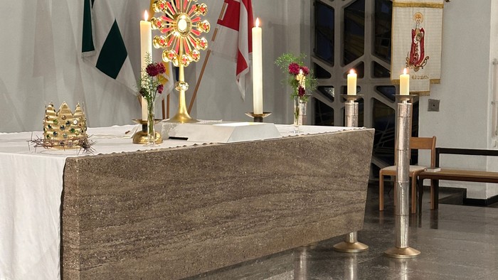 Eleganter Kirchenaltar, geschmückt mit Kerzen, Fahnen, Blumengestecken und religiösen Verzierungen auf einem Marmorboden.