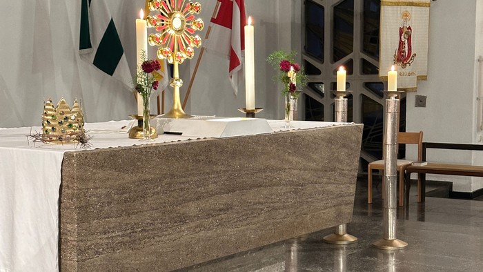 Eleganter Kirchenaltar, geschmückt mit Kerzen, Fahnen, Blumengestecken und religiösen Verzierungen auf einem Marmorboden.