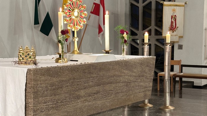 Eleganter Kirchenaltar, geschmückt mit Kerzen, Fahnen, Blumengestecken und religiösen Verzierungen auf einem Marmorboden.