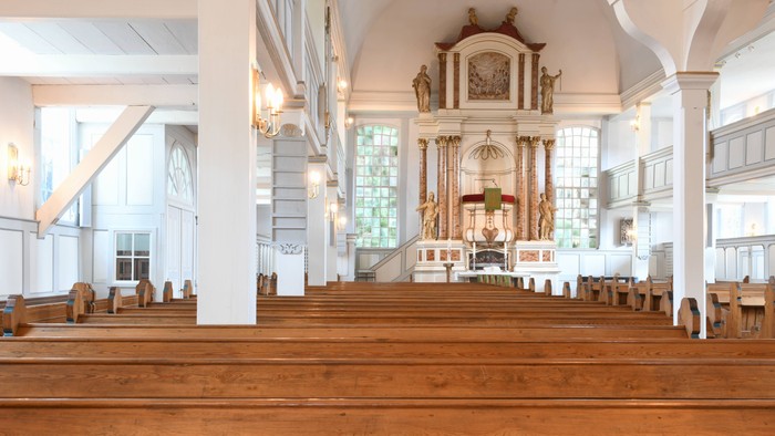 Große, helle Kirche mit hölzernen Kirchenbänken und einem Altar im Hintergrund