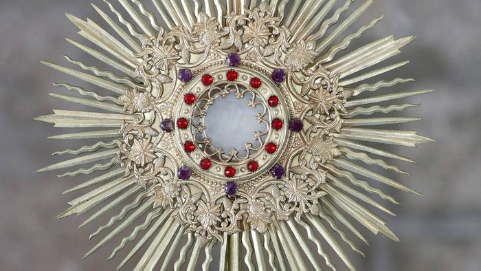 Ein verzierter goldener Monstranz mit roten Edelsteinen und einem centralen Glasfenster.