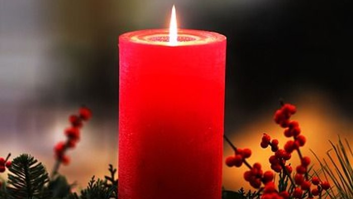 Eine rote Kerze brennt in einem Kranz aus Tannenzweigen und Beeren.
