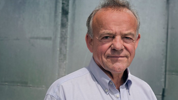 En smilende middelalderlig mand med kort hår og en lysblå skjorte.