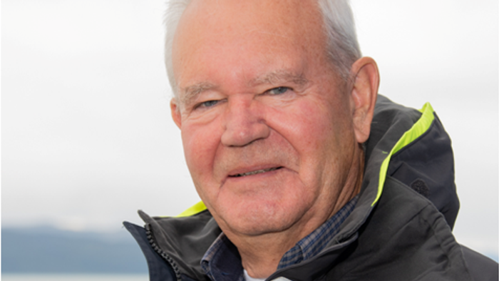 En aldermand med en svart og grøn jacke står ved stranden