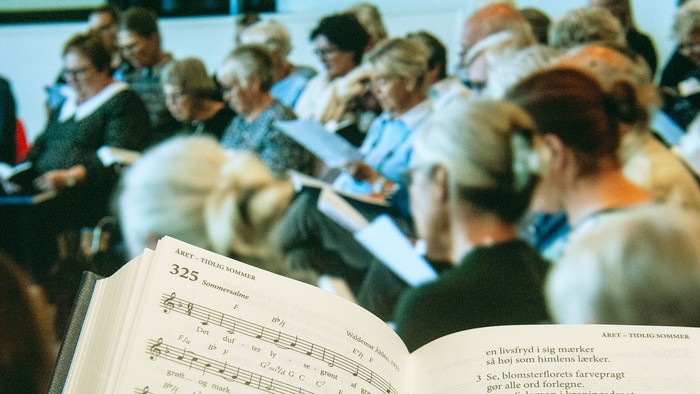 En gruppe af mennesker synger i kor, mens de holder partiture med noter.