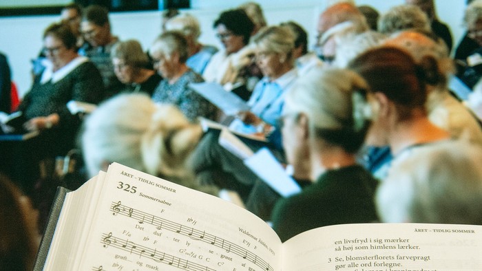 En gruppe af mennesker synger i kor, mens de holder partiture med noter.