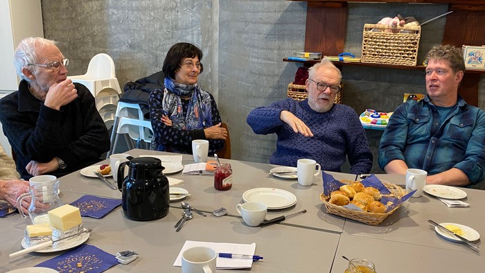 Mennesker omkring bord drikker kaffe og spiser boller