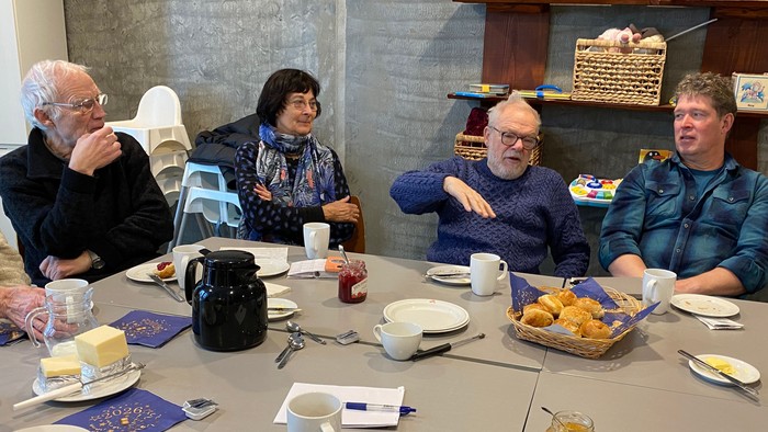 Mennesker omkring bord drikker kaffe og spiser boller