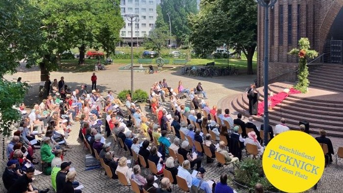 Plakat für eine Open-Air-Pfingstgottesdienst-Veranstaltung mit einer Menschenmenge, die sich auf einem Platz zu einer religiösen Feier versammelt.