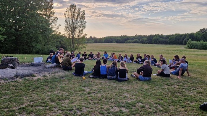 En gruppe af mennesker sidder i en cirkel på en eng ved solnedgang