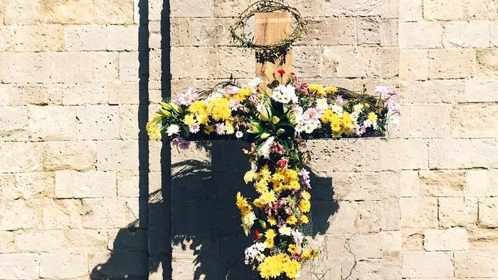 A woman kneels before a large floral sculpture against a stone wall.