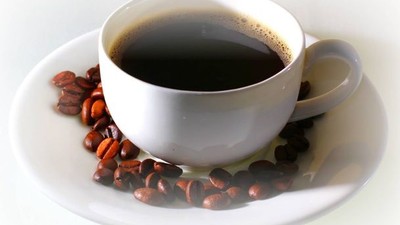 A cup of black coffee on a saucer surrounded by coffee beans