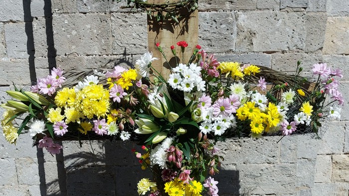 Cross decorated with flowers against stone wall