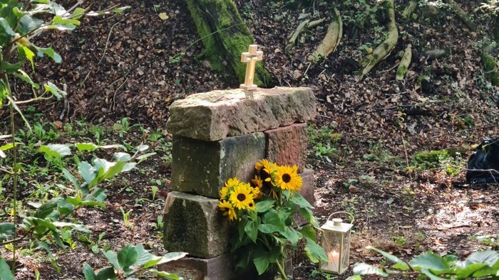 Ein steinernes Kreuz als Grabmal mit Sonnenblumen und einer Laterne.