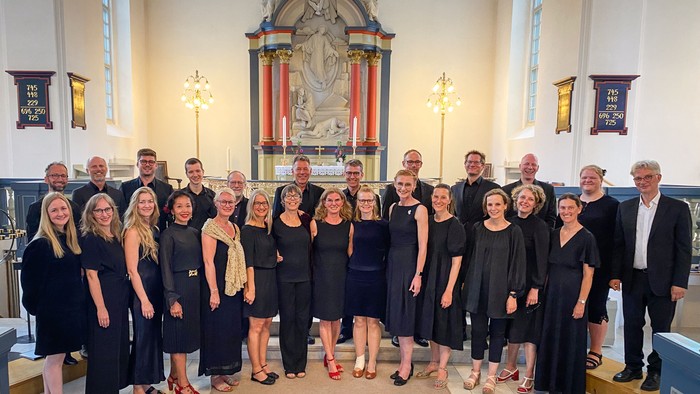 En gruppe sangere og musikere poserer formelt inde i en stor kirke med prægtige dekorationer.