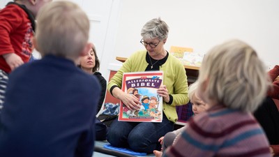 En kvinde læser et børnebog til en gruppe børn.