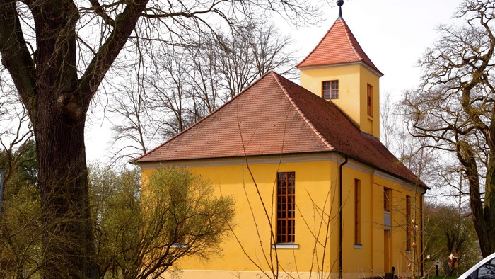 Kleine gelbe Kirche mit rotem Dach in ländlicher Umgebung