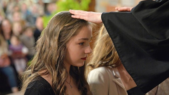 Eine Frau bekommt von jemandem eine schwarze Mütze aufgesetzt, während Zuschauer zusehen.