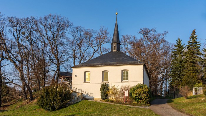 Weiße Kirche mit schwarzem Turm und goldener Spitze, umgeben von Bäumen und Gras.