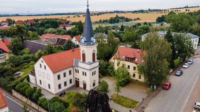 Kirchliches Gebäude mit hohem Turm in kleinem Dorf, umgeben von Grünflächen und Häusern