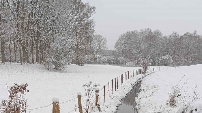Verschneiter Pfad neben einem zugefrorenen Bach und einem Stacheldrahtzaun