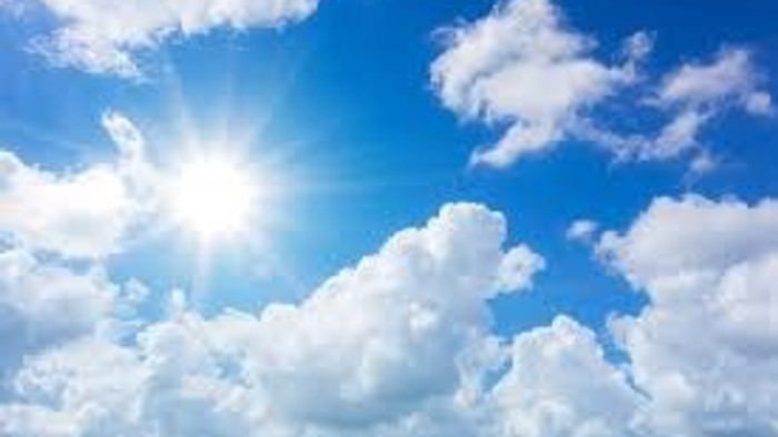 Helle Sonne scheint durch verstreute, flauschige weiße Wolken vor einem klaren blauen Himmel.