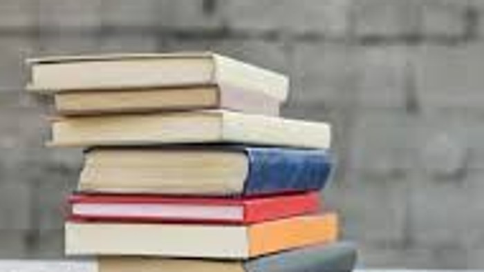 Ein Stapel bunter Bücher, der auf einem Tisch vor einer strukturierten Wand platziert ist.