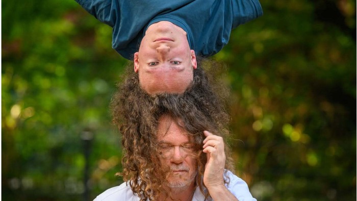 Zwei Männer, einer über Kopf mit langen Locken, die dem anderen Mann ins Gesicht fallen