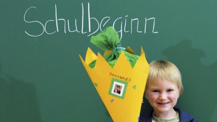Ein kleiner Junge hält einen gelben Blumenstrauß vor einer Tafel mit der Aufschrift 