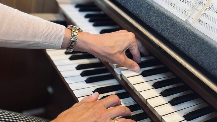 En person spiller piano med noter på pulpet.