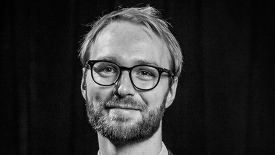 En svart-hvid portrætfoto af en mand med briller og skæg.