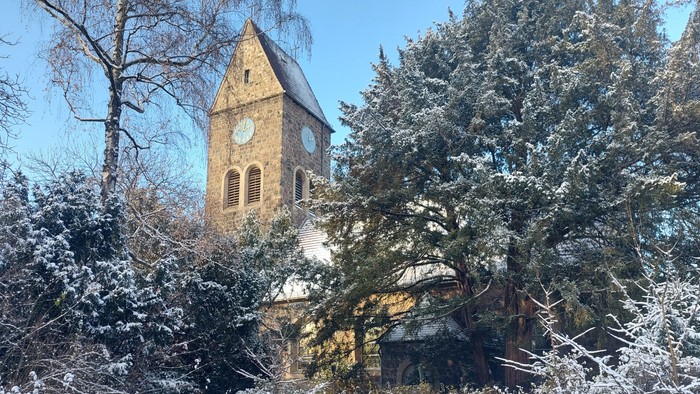 Schneebedeckte Bäume und ein Kirchturm mit Uhr im Winter